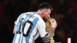 El delantero argentino Lionel Messi (n.º 10) sostiene el Balón de Oro al mejor jugador mientras besa el trofeo de la Copa Mundial de la FIFA durante la ceremonia de premiación, tras la final del Mundial de Qatar 2022