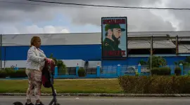 Una mujer en una patineta eléctrica, frente a una fábrica que exhibe una imagen del fallecido, el líder cubano Fidel Castro