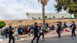 Migrantes esperan en la acera antes de ser registrados en el distrito de Loma Colmenar de Ceuta el 31 de agosto de 2026.