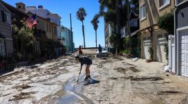 Una mujer palea la arena arrastrada por la marejada ciclónica en una calle de Long Beach, California