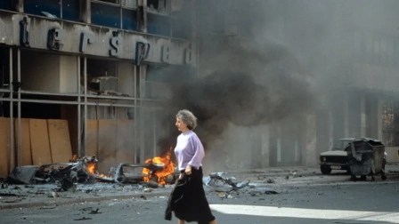Una mujer corre ante un edificio bombardeado en Sarajevo