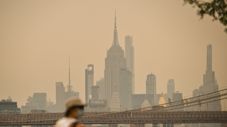 Una persona con el rostro cubierto camina cerca del Puente de Brooklyn mientras el humo de los incendios forestales provenientes de Canadá provoca una densa neblina el 16 de julio de 2026 en Nueva York.