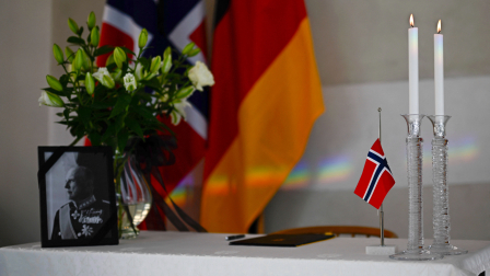 Un retrato del difunto rey noruego Harald V, adornado con una cinta negra de luto, se exhibe junto a flores, velas encendidas, Una bandera noruega y un libro de condolencias, frente a las banderas noruega y alemana, en la Embajada Real de Noruega en Berlín